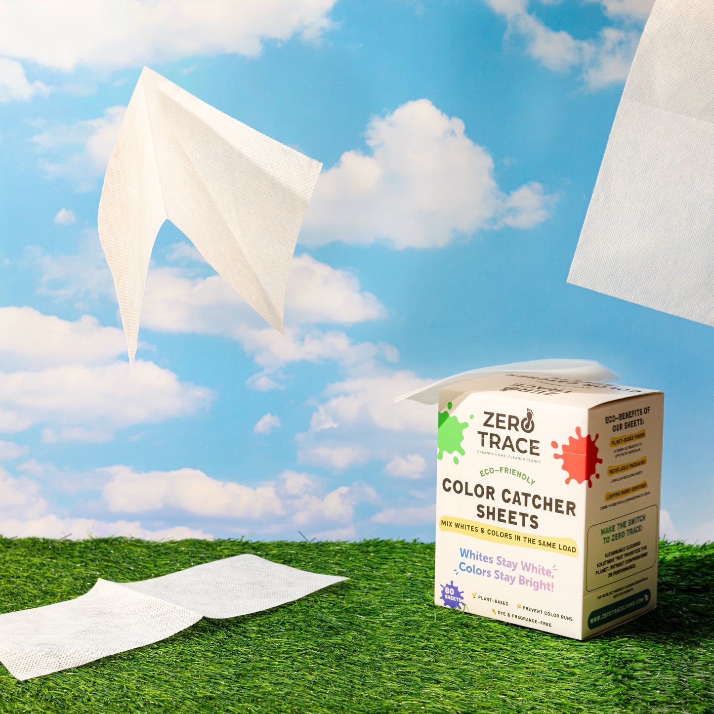 A box of Zero Trace Color & Dye Protector Sheets rests on grass as two sheets float in the air against a blue, cloud-streaked sky, showcasing their color run prevention benefits.