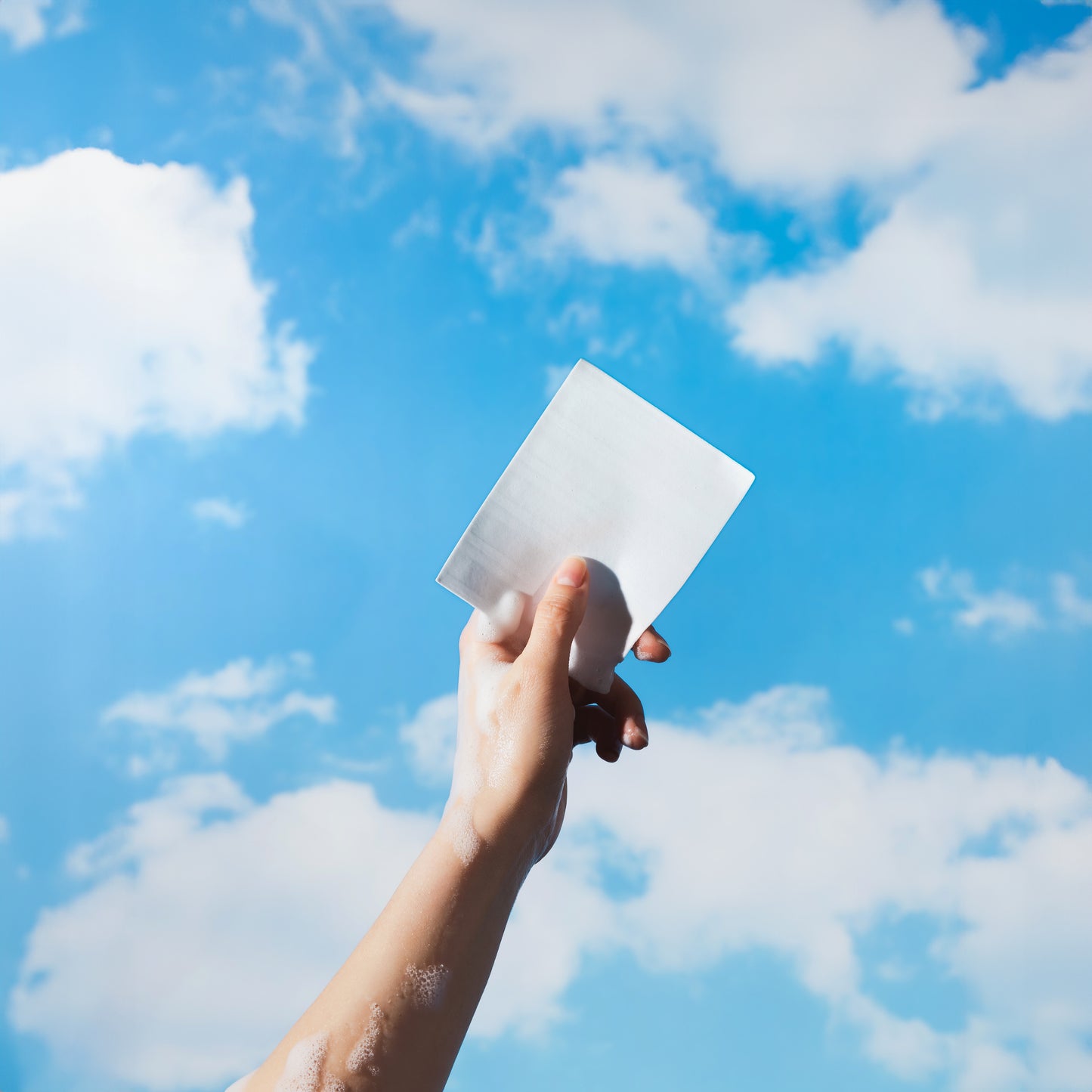 An eco-friendly Zero Trace hand holding a piece of Hand Soap Sheets against a blue sky.