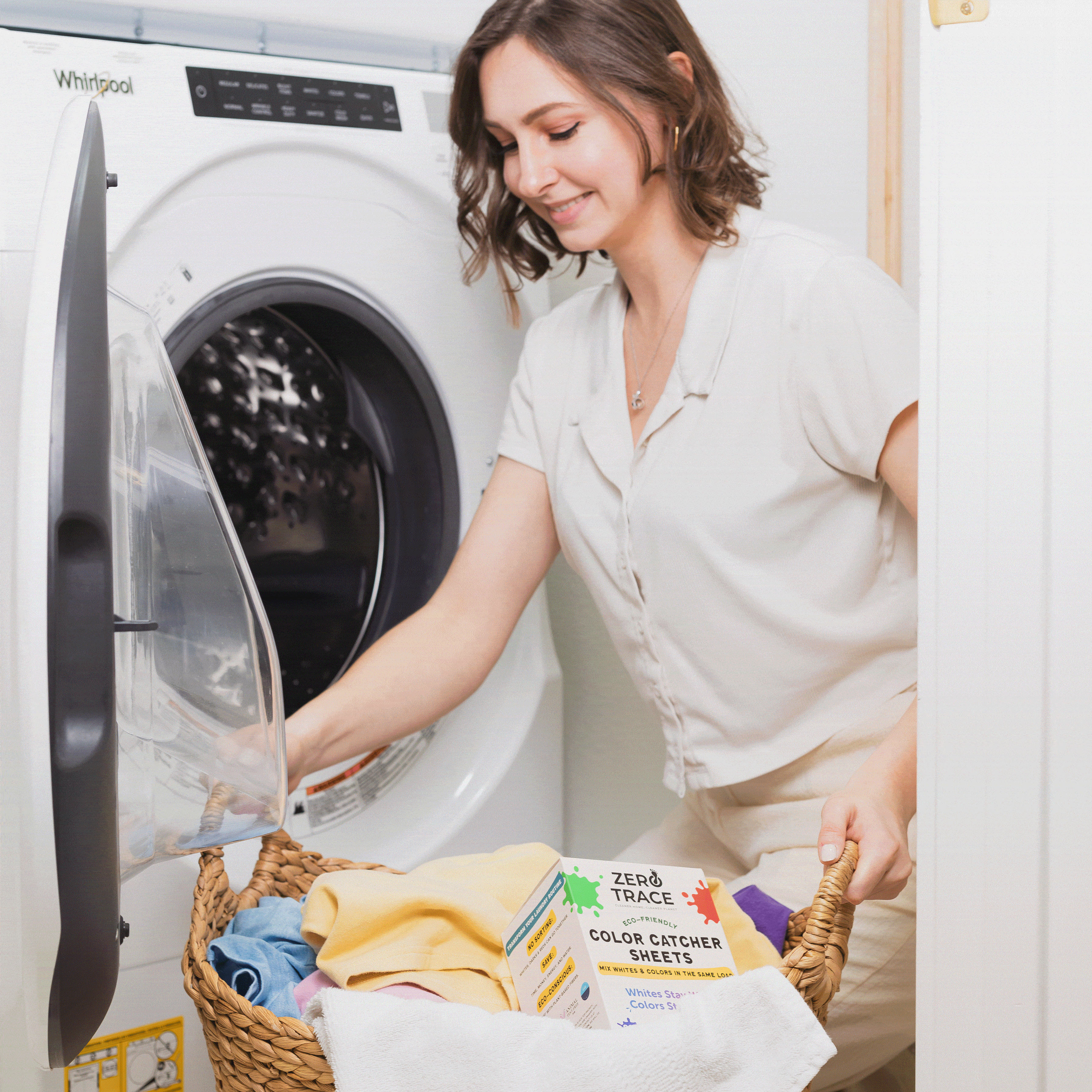 A woman is putting laundry in a basket in front of a washing machine while using Zero Trace Color Catcher Sheets.
