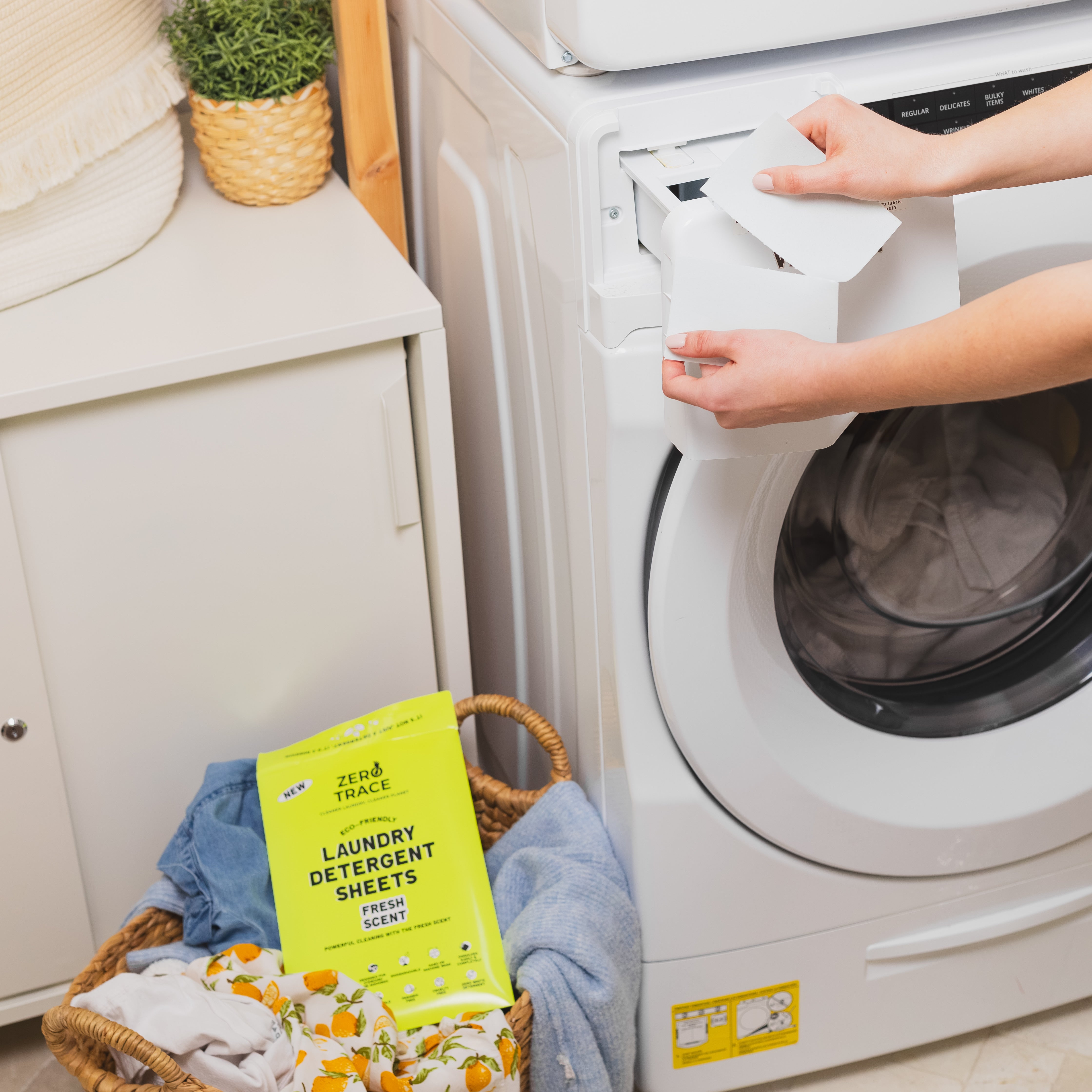 A woman is putting Zero Trace laundry detergent sheets into a washing machine.
