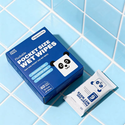 A box and packet of Zero Trace FLUSHABLE MINI WIPES with a panda design rest on blue and white tiles—eco-friendly, pocket-sized, and perfect for sensitive skin on the go.